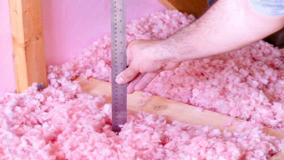 Checking the energy efficiency of their house by measuring the thickness of fiberglass insulation in the attic